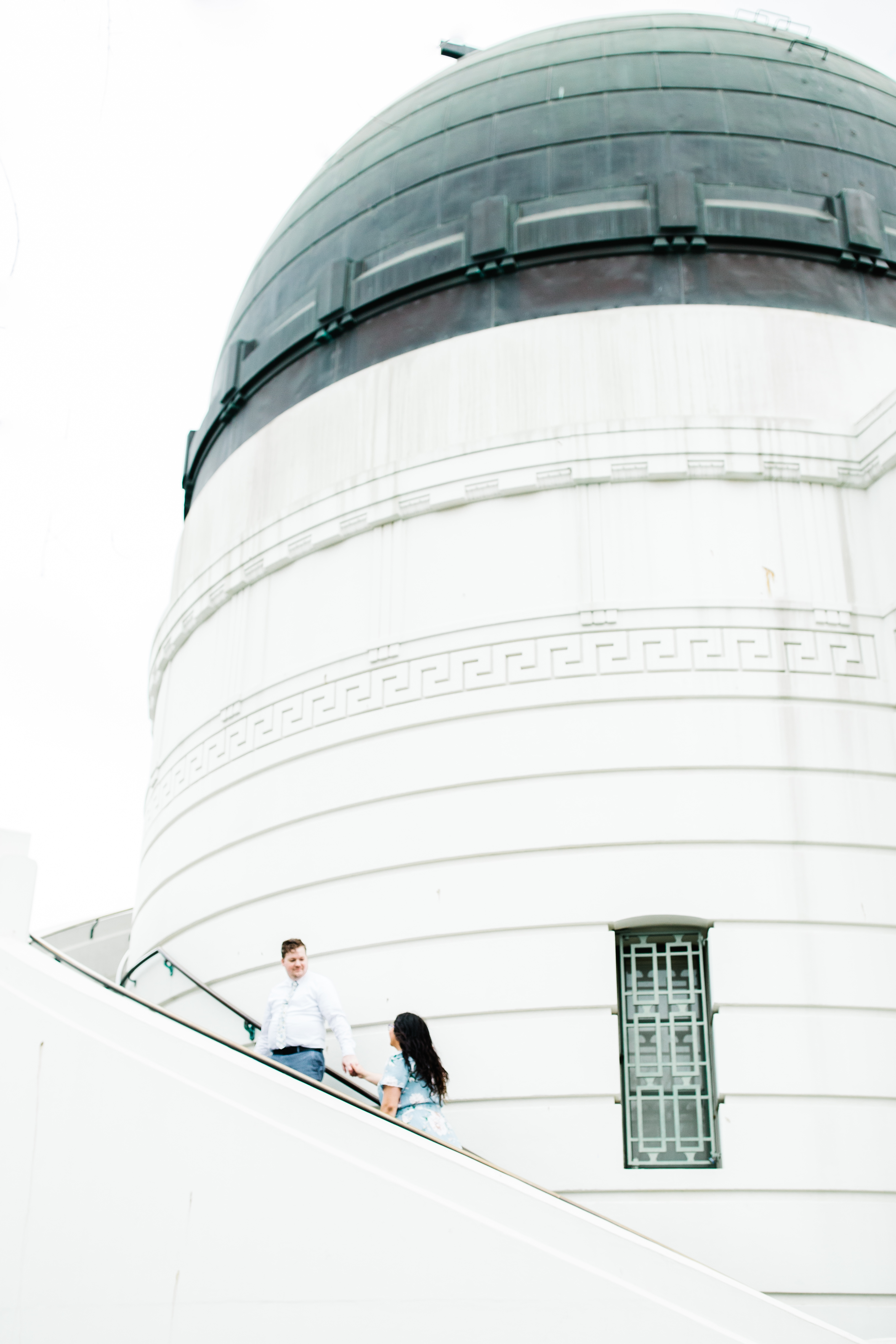 griffith observatory engagement photos Couple walking toward up stairs at Griffith Observatory in Los Angeles , California with observatory dome in the background.