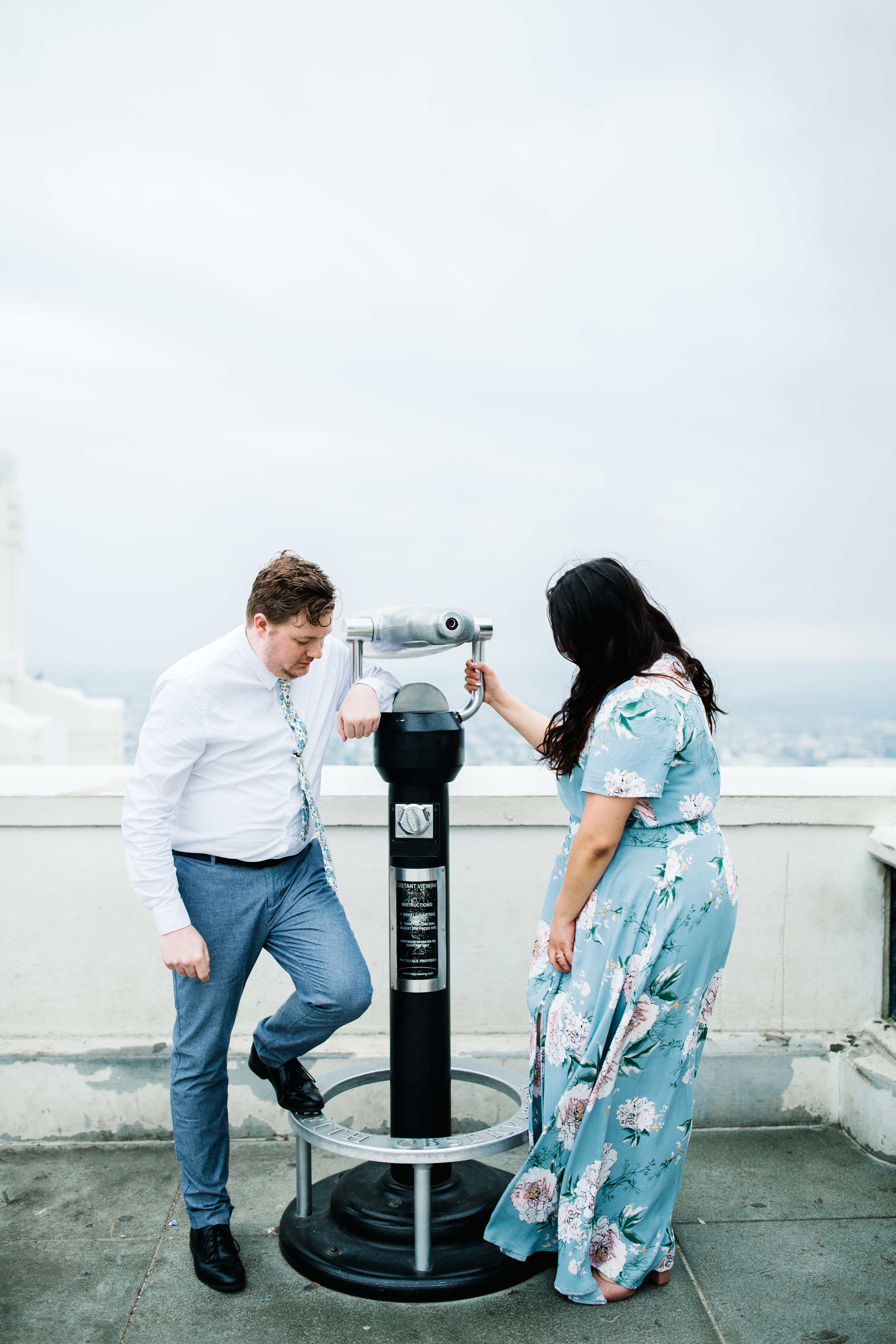 griffith observatory engagement photos Couple stand at viewing scope at Griffith Observatory in Los Angeles , California.
