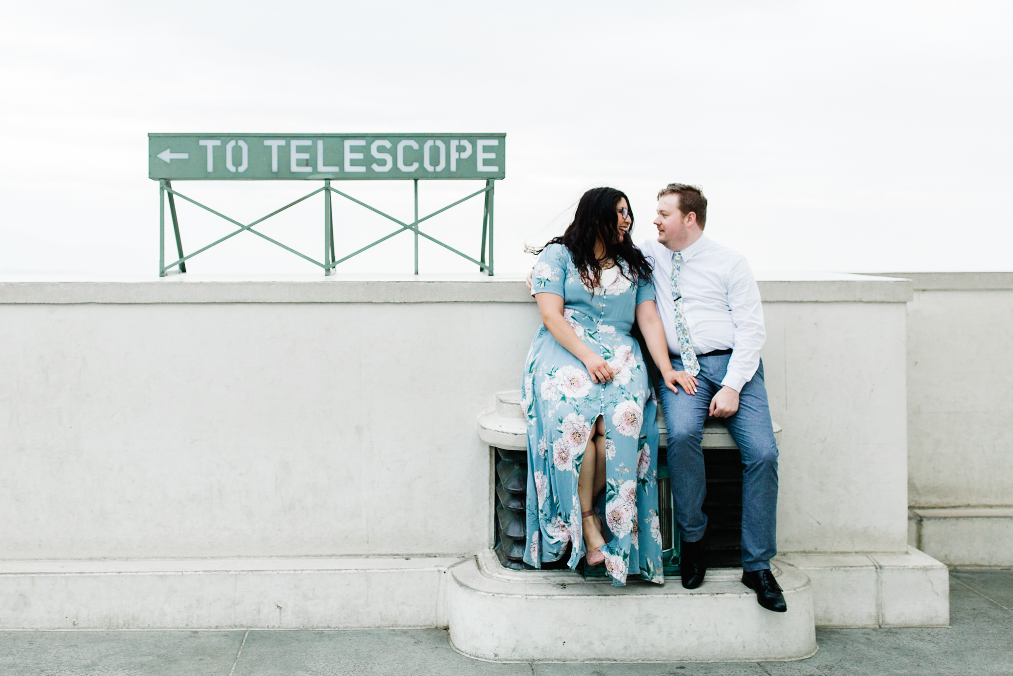 griffith observatory engagement photos Couple sits next to telescope sign at Griffith Observatory in Los Angeles , California.