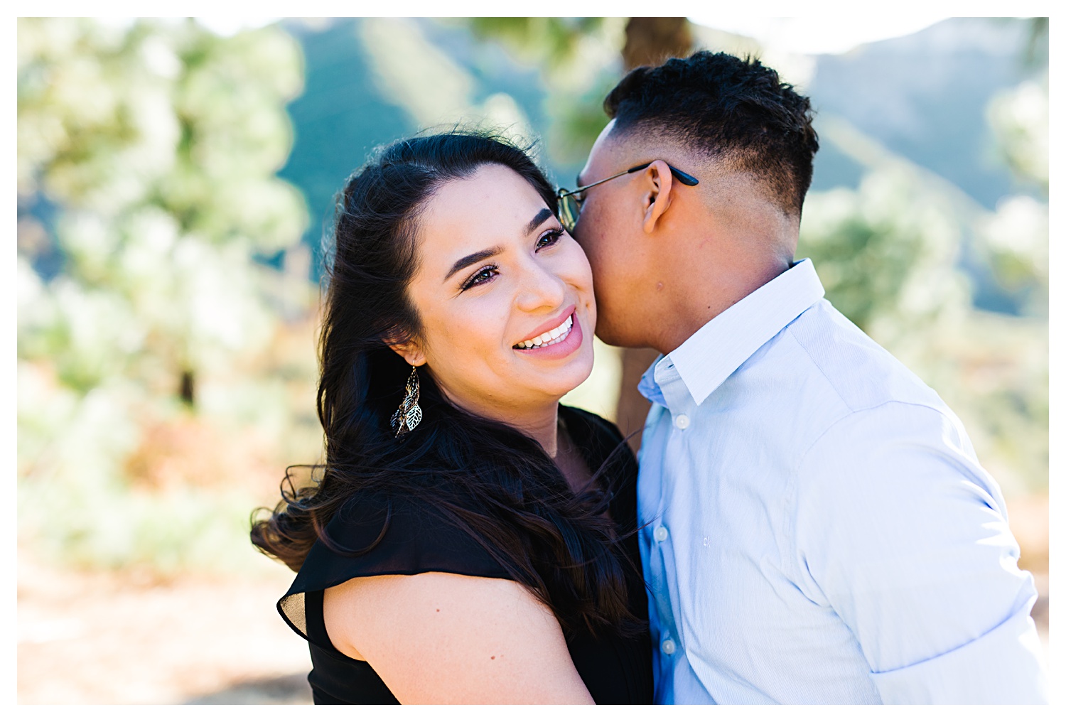 guy kissing whispering to girl with trees in the background Angeles National Forest Engagement Photos